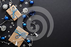 Christmas gifts with blue ribbon, blue balls, fir tree branches, cones, confetti on dark black background with copy space. Flat