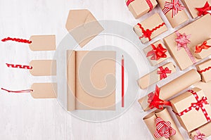 Christmas gifts boxes, blank labels and notepad for your text of kraft paper with red bows and ribbon on soft white wood board.