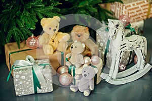 Cute little boy sitting down by the decorated Christmas tree with toys, teddy bears and gift boxes