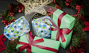 Christmas gifts packaged and decorated with bows, green and red tinsel on wooden background and a golden star