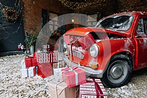 Christmas gifts packed with red,white,craft paper and tapes under decorated retro red car with trunk full of New Year gifts on