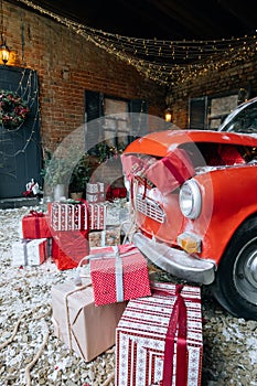 Christmas gifts packed with red, white, craft paper and tapes under decorated retro red car with trunk full of New Year gifts on