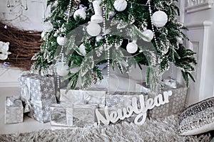 Christmas gifts packed with silver and white paper and tapes under decorated tree.