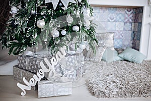 Christmas gifts packed with silver and white paper and tapes under decorated tree.