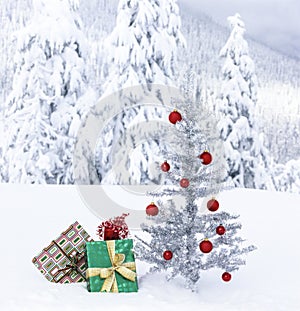Christmas gifts under artificial tinsel tree outdoors with snowy mountain landscape background.  Actual photo shot in winter