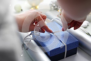 Christmas  gifts. A woman wraps a present under a Christmas tree in silver paper.