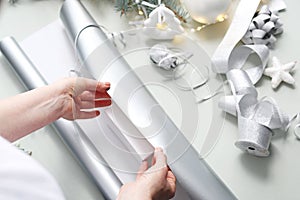 Christmas gifts. A woman wraps a present under a Christmas tree in silver paper.