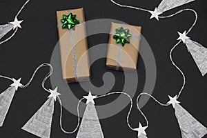 Christmas gifts wrapped in kraft paper. Two  bow green and silver colors. Garland from herringbone. Black background, top view,