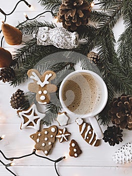 Christmas gingerbread cookies, coffee cup and fir branches on white rustic wooden table with lights