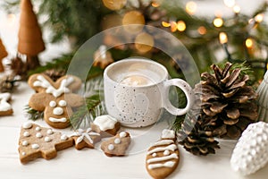 Christmas gingerbread cookies, coffee, pine cones  and warm lights on white wooden table