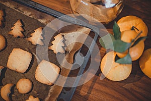 Christmas gingerbread cookies in the form of fir trees on a pan next to oranges on a wooden table.