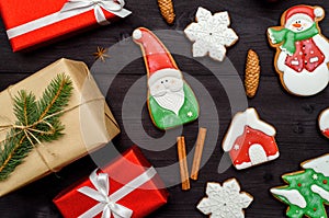 Christmas gingerbread cookies, gift boxes, cinnamon, cones, fir tree branches on dark wooden background, copy space.