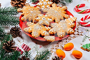 Christmas gingerbread cookies homemade on red plate with branches of Christmas tree and decor on home New Year table. Merry Christ