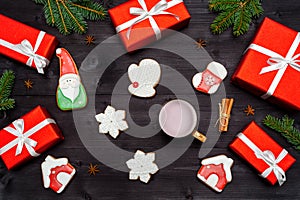 Christmas gingerbread cookies, one cup of hot cocoa, red gift boxes, fir tree branches on dark wooden background, copy space.