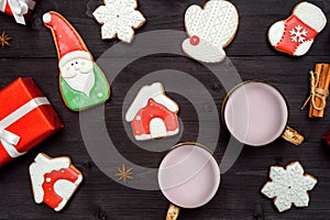 Christmas gingerbread cookies, two cups of hot cocoa, red gift box, cinnamon and star anise on dark wooden background.