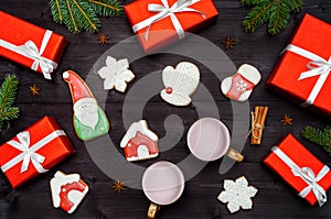 Christmas gingerbread cookies, two cups of hot cocoa, red gift boxes, fir tree branches on dark wooden background, copy space.