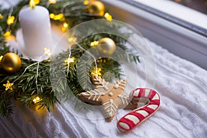 Christmas gingerbread in form of star and caramel cane near festive decoration with golden balls, white candle and warm garland li