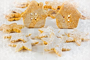 Christmas gingerbread house, stars and linzer cookies on white wood background, candle light, frosted ice floral texture vignette