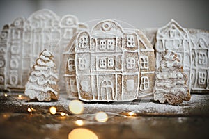 Christmas gingerbread houses and tree in snow on rustic wooden table with golden lights. Christmas cookies village scene.