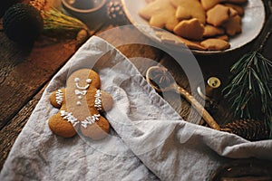 Christmas gingerbread man cookie on rustic table with candle, napkin, decorations, spices. Atmospheric moody image. Making stylish