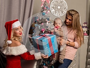 Christmas girl giving presents to little baby. woman dressed as Santa Claus