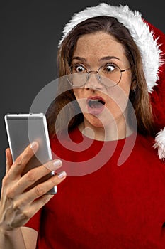 Christmas girl with santa claus hat and mobile phone. Looks surprised