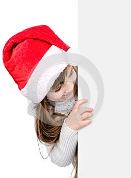 Christmas girl in santa helper hat looks out from behind a white banner. isolated on white background
