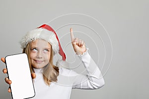 Christmas girl Santa pointing up and holding smartphone with blank empty white screen display on white banner background