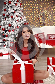 Christmas girl winter portrait. Beautiful santa woman open present gift box. Happy laughing brunette in red with long hair sitting