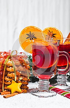 Christmas glass of red mulled wine on table with cinnamon sticks, branches of Christmas tree, snow,