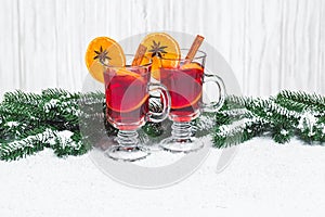 Christmas glass of red mulled wine on table with cinnamon sticks, branches of Christmas tree, snow,