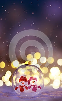 Christmas glass transparent ball with a snowmen inside on snow. Christmas lights glitter background