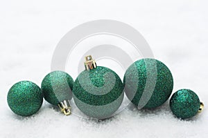 Christmas glitered green baubles, balls isolated on snow. Winter greeting card with copy space