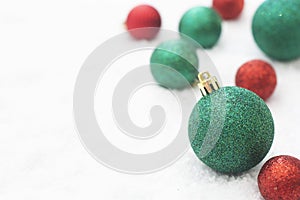 Christmas glitered green and red baubles, balls isolated on snow. Winter greeting card with copy space