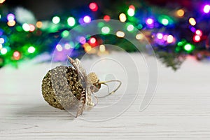 christmas golden ball toy on background of colorful garland lights. stylish rustic white wooden table. space for text. holiday gr