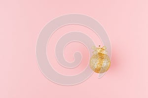 Christmas golden decoration as simple festive bright background - gold glittering ball with ribbon on pastel pink color, top view.