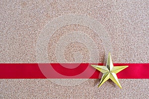 Christmas golden star and red ribbon on cork board.