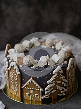 Christmas gray cake decoraited of gingerbread cookies in shape of homes and snowy christmas trees, marshmallows