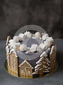 Christmas gray cake decoraited of gingerbread cookies in shape of homes and snowy christmas trees, marshmallows