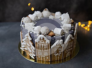 Christmas gray cake decoraited of gingerbread cookies in shape of homes and snowy christmas trees, marshmallows, snowflakes,