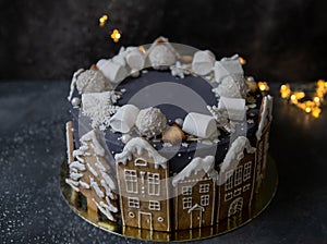 Christmas gray cake decoraited of gingerbread cookies in shape of homes and snowy trees, marshmallows, snowflakes, sweets.