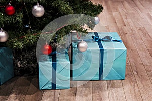 Christmas green tree with decorations and presents under it in loft interior. Large blue boxes in a gift wrap with a ribbon. real