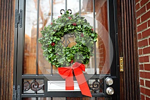 Christmas green wreath with red ribbon on the front door. Entrance to the house decorated for the winter holiday - Xmas and New