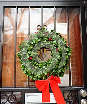 Christmas green wreath with red ribbon on the front door. Entrance to the house decorated for the winter holiday - Xmas and New