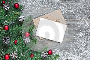 Christmas greeting card with fir branches, red decorations and pine cones on rustic wooden table covered with snow