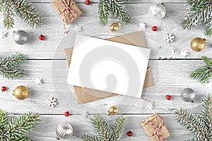 Christmas greeting card in frame made of fir tree, gift boxes, decorations on white wood background. Flat lay