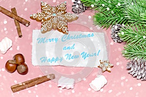 Christmas greeting card over wooden light pink table with snow fir tree, snowflakes, nuts, marshmallow and cinamon.