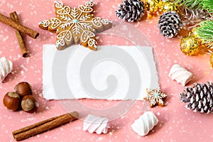Christmas greeting card over wooden light pink table with snow fir tree, snowflakes, nuts, marshmallow and cinamon.