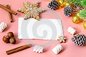 Christmas greeting card over wooden light pink table with snow fir tree, snowflakes, nuts, marshmallow and cinamon.