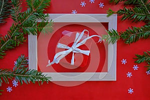 Christmas greeting card with red gift box ribbon in frame across christmas tree branch and tinsels on red background. Top view